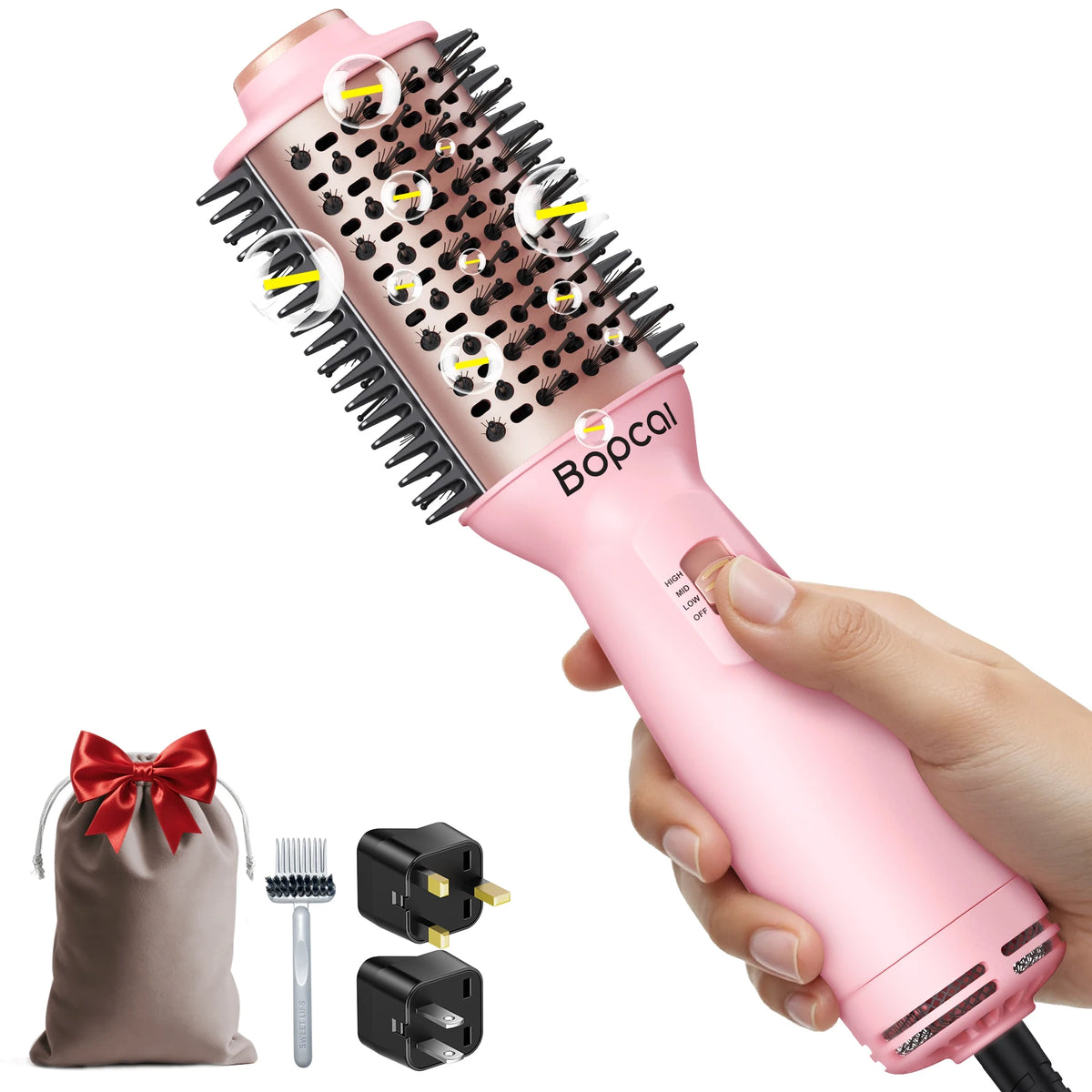 Pink hot air styling brush shown with a beige drawstring travel bag, cleaning brush, and two black power adapters on a white background. Copy